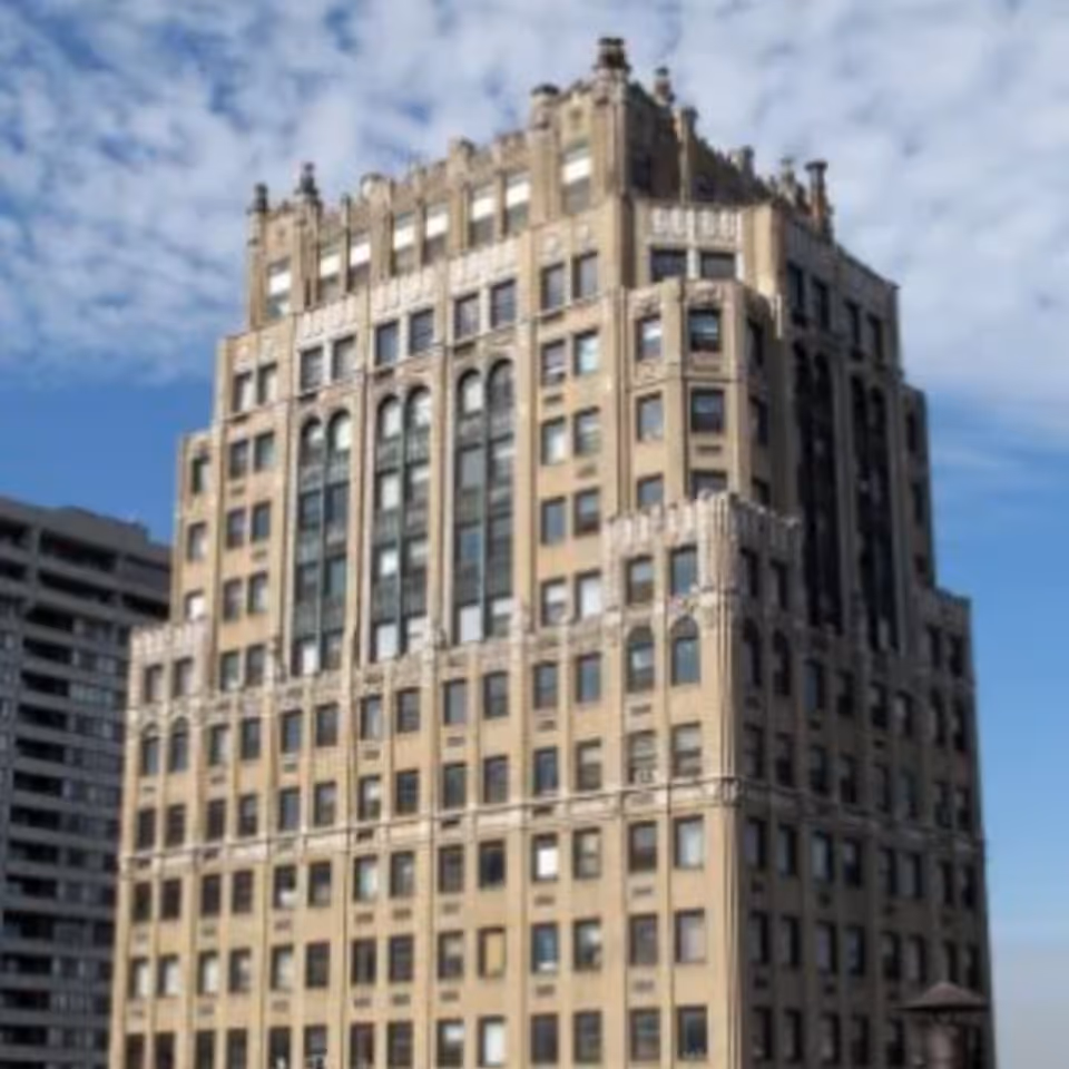 Ornate multi-story beige masonry apartment building with decorative cornices against a blue sky.