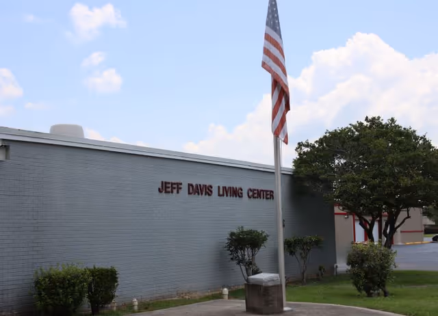 Exterior front of the Jeff Davis Living Center building with an American flag on a flagpole and surrounding shrubs.