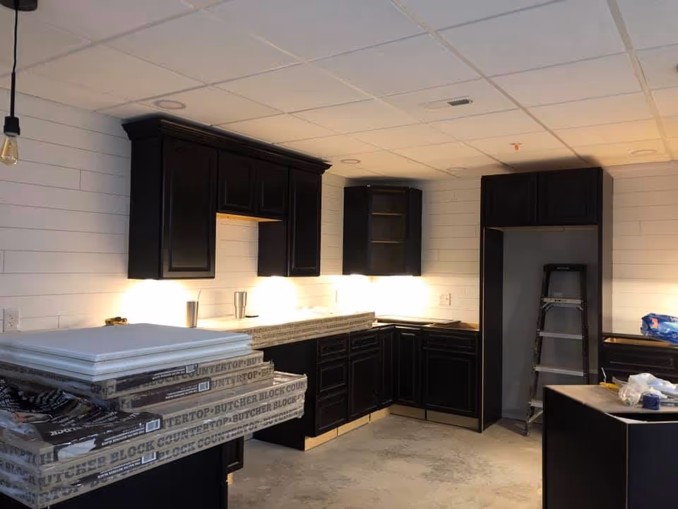 Under-construction kitchen with dark cabinets, stacked countertop materials and a ladder.