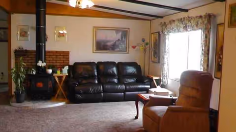 Cozy living room with black leather sofa, recliner, fireplace, and large window curtains.