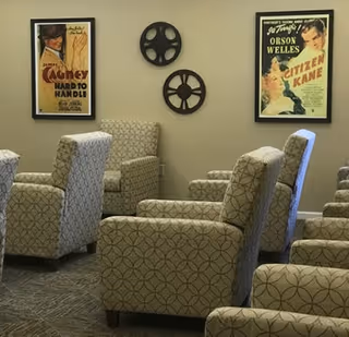 Rows of patterned upholstered armchairs face a wall decorated with vintage movie posters and two decorative film reels.