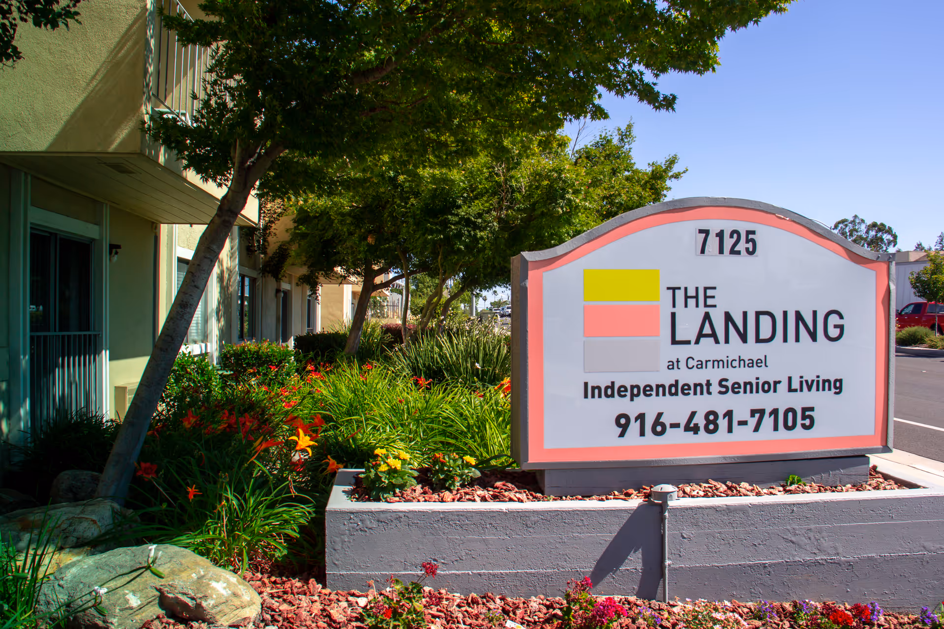 Exterior sign for The Landing at Carmichael beside landscaped entrance and greenery.