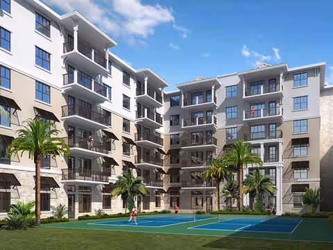 Multi-story residential building surrounding a landscaped courtyard with palm trees and a tennis court with people playing.