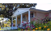 Front view of a brick senior care building with white columns, a porch, an American flag, and colorful flower beds in the foreground.