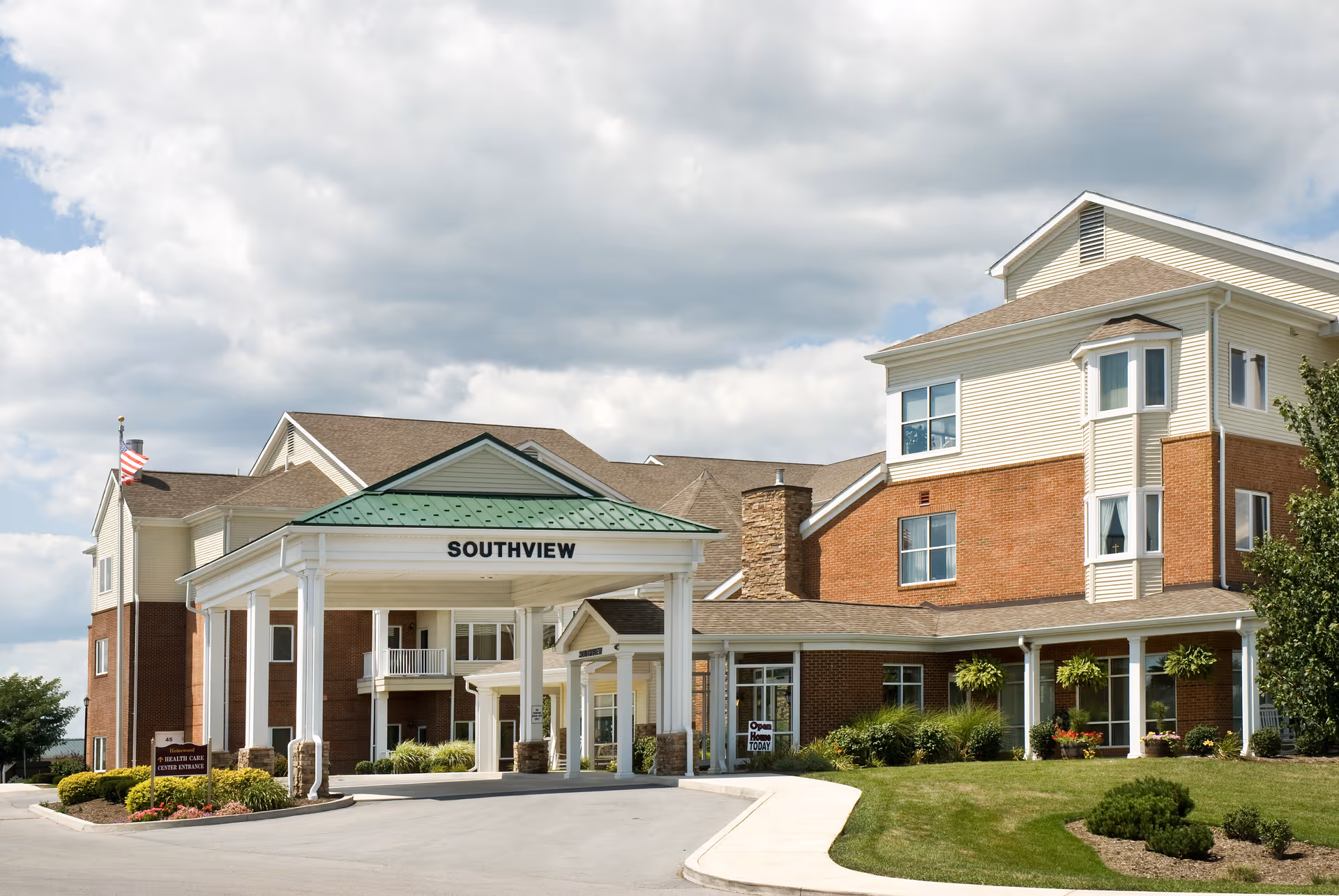 Exterior view of a senior living facility named Southview with a covered entrance, brick and siding facade, well-maintained landscaping, and an American flag on a flagpole.