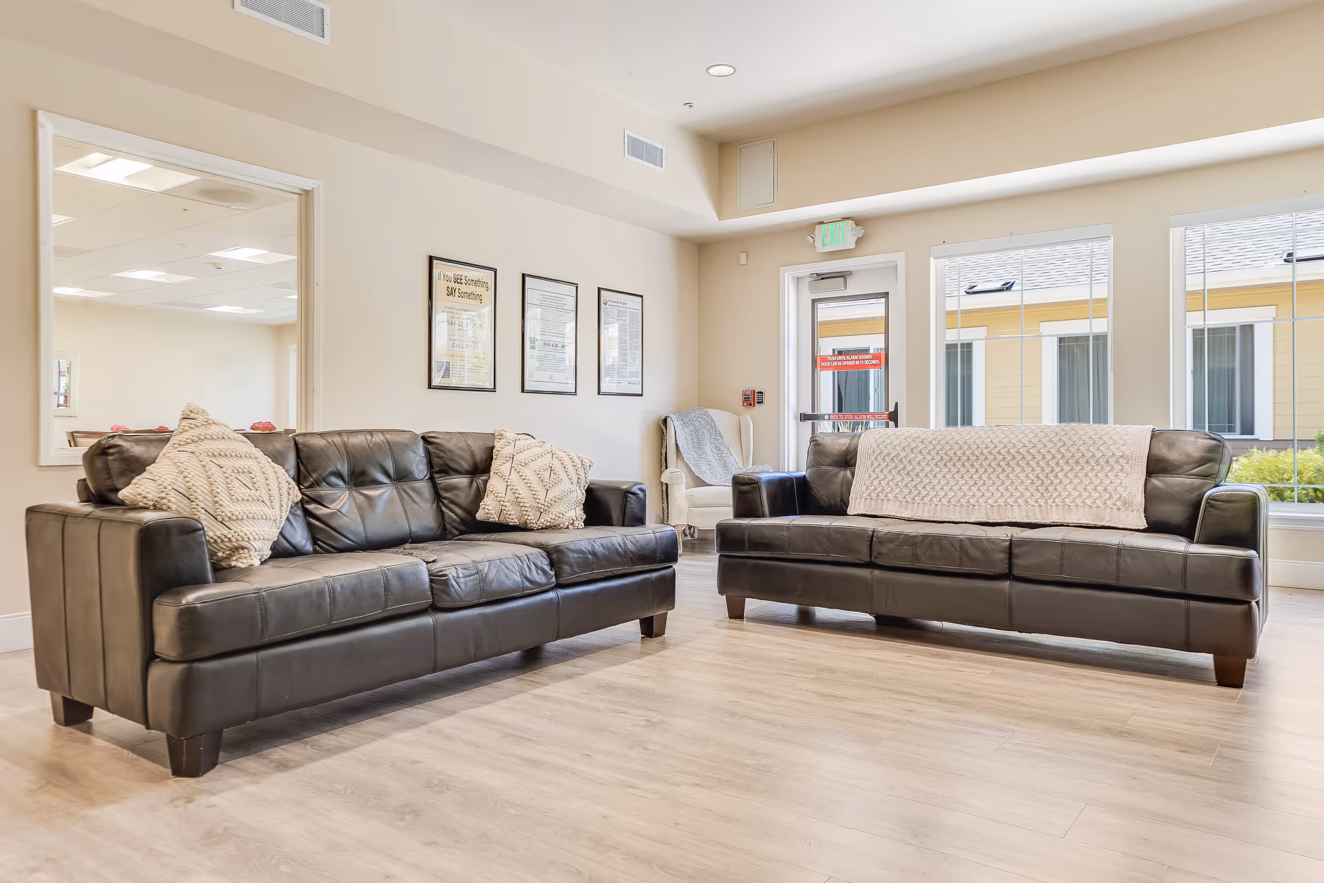 Bright common living area with two black leather sofas, throw pillows, hardwood floors and large windows.
