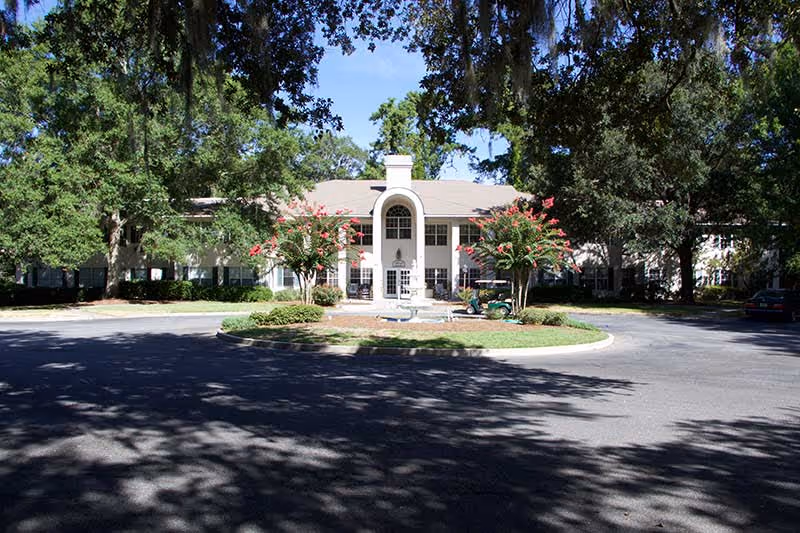 Front exterior of Magnolia Manor with a central columned entrance, circular driveway, and trees surrounding the building.