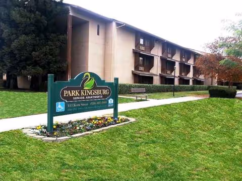 Park Kingsburg Senior Apartments sign beside a beige multi-story building and green lawn.