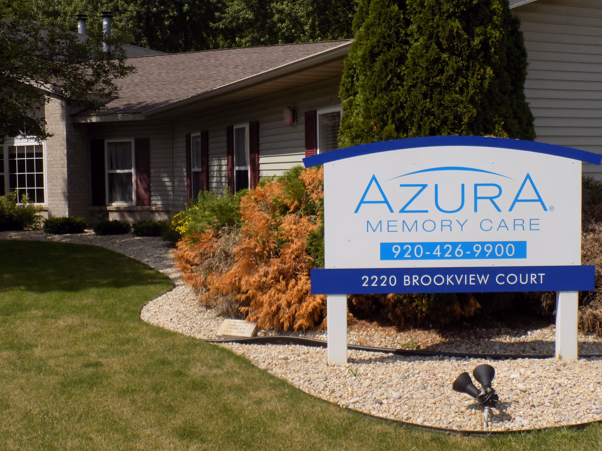 Sign for Azura Memory Care in front of the facility with landscaping and a lawn.