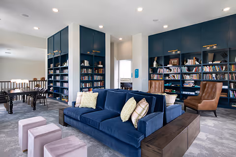 Bright communal lounge with a blue velvet sofa, bookshelves, armchairs, and tables.