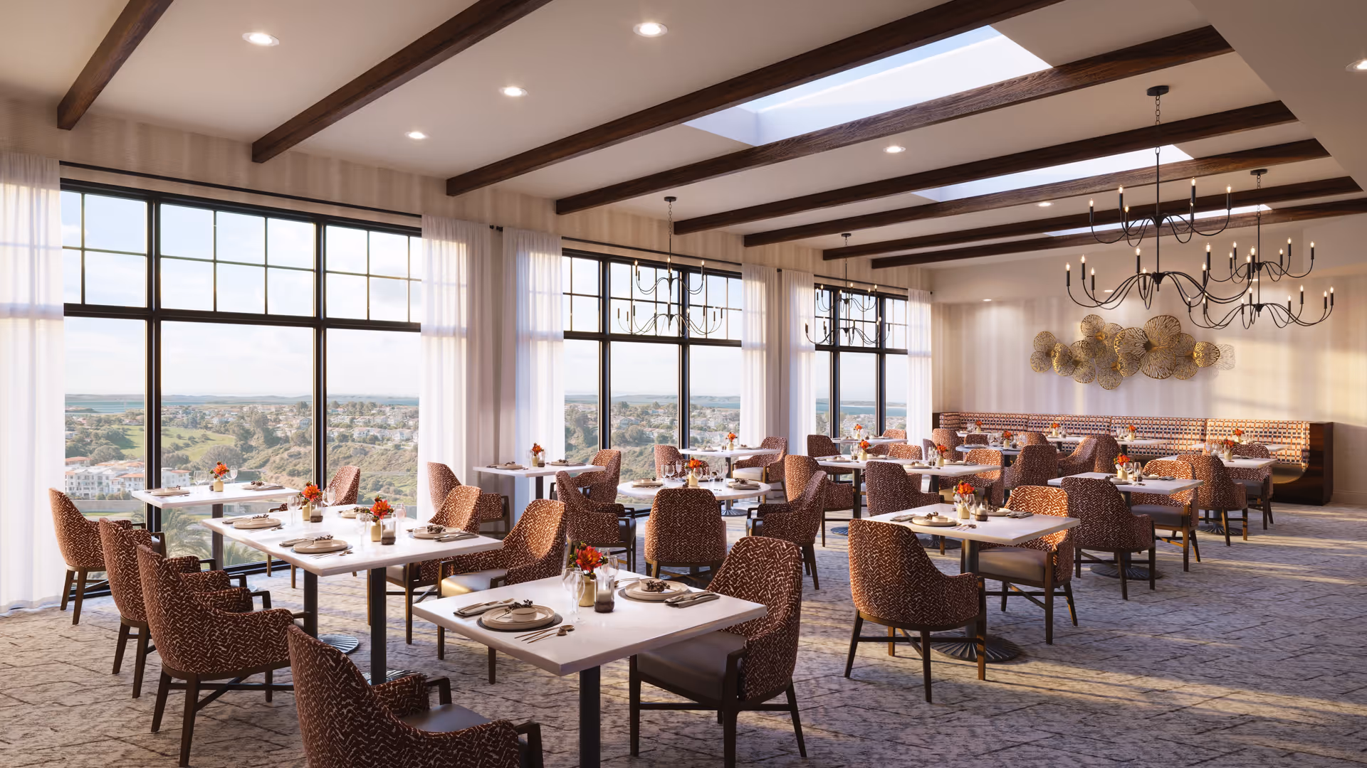 Bright dining room with multiple set tables and upholstered chairs, large windows showing a scenic view, chandeliers, and exposed ceiling beams.