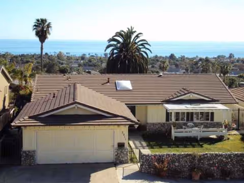 Front exterior of a brown-tiled house with palm trees and ocean view.