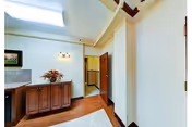 Interior corridor showing wooden cabinetry topped with flowers, a skylight, a rug on hardwood floors, and an open doorway.