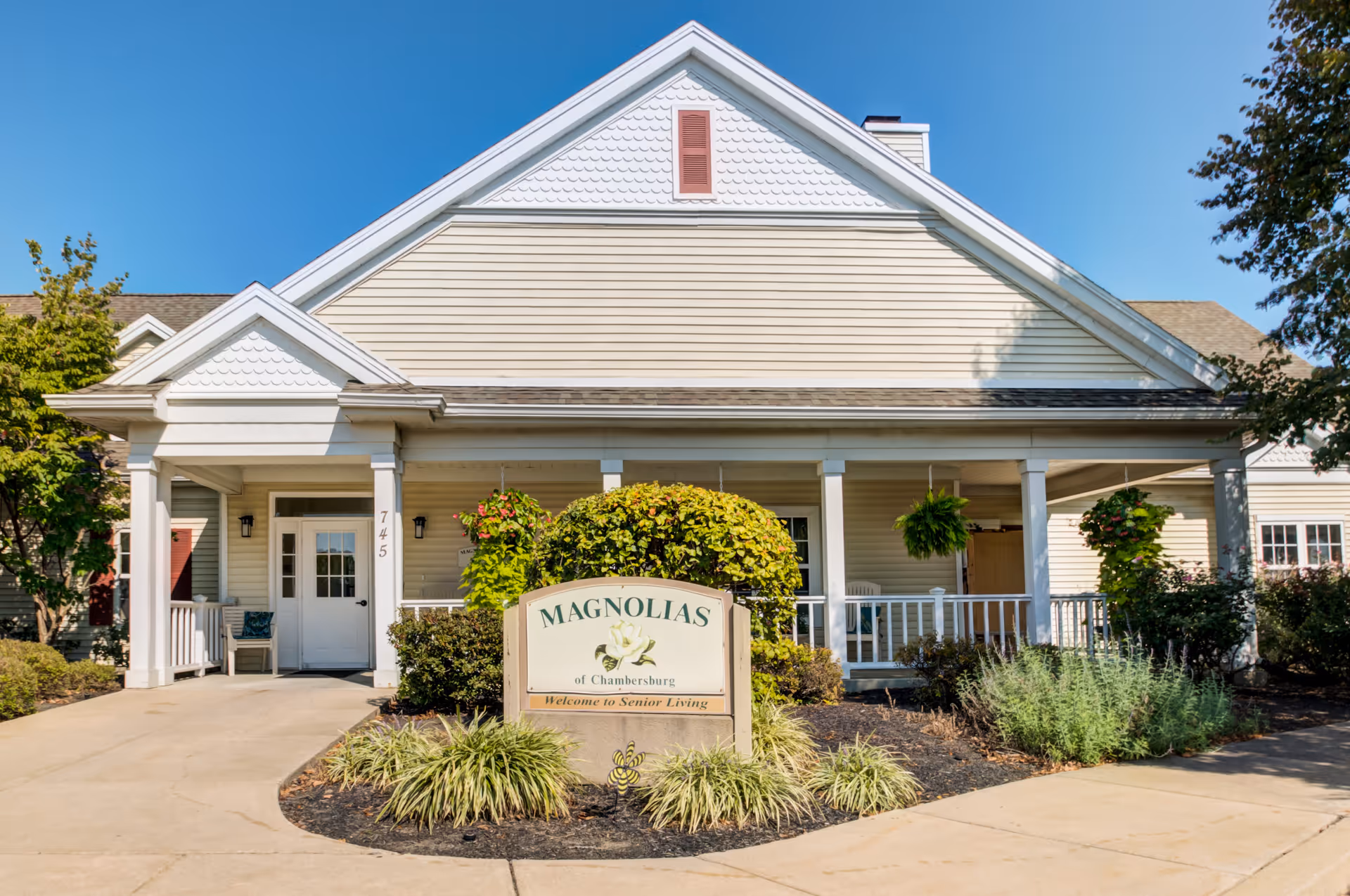 Front exterior of the Magnolias of Chambersburg senior living building with a covered porch and landscaped sign.