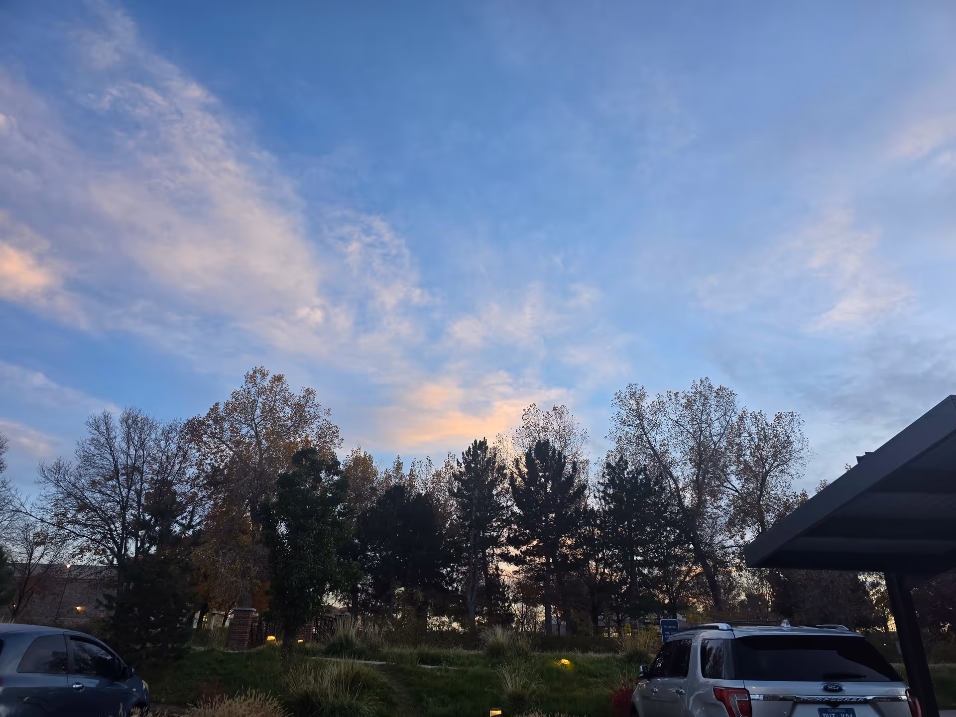 Outdoor parking area at Hyland Hills Senior Living during dusk with several cars parked, trees in the background, and a partly cloudy sky with soft evening light.