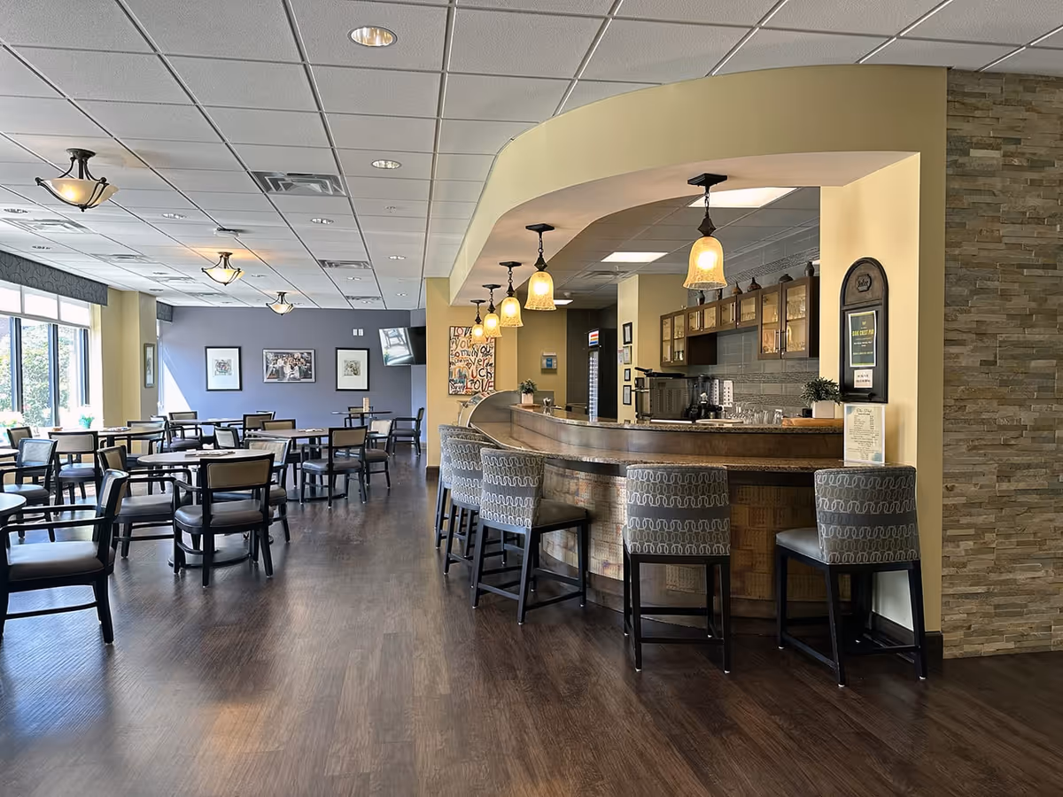 Spacious dining room with tables and chairs and a curved bar with stools and hanging pendant lights.