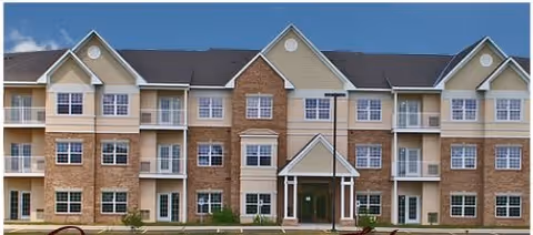 Three-story brick and siding residential building with balconies and a central entrance under a blue sky.