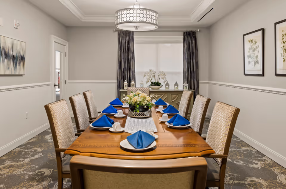 Formal dining room with a long wooden table set with blue napkins and eight upholstered chairs.