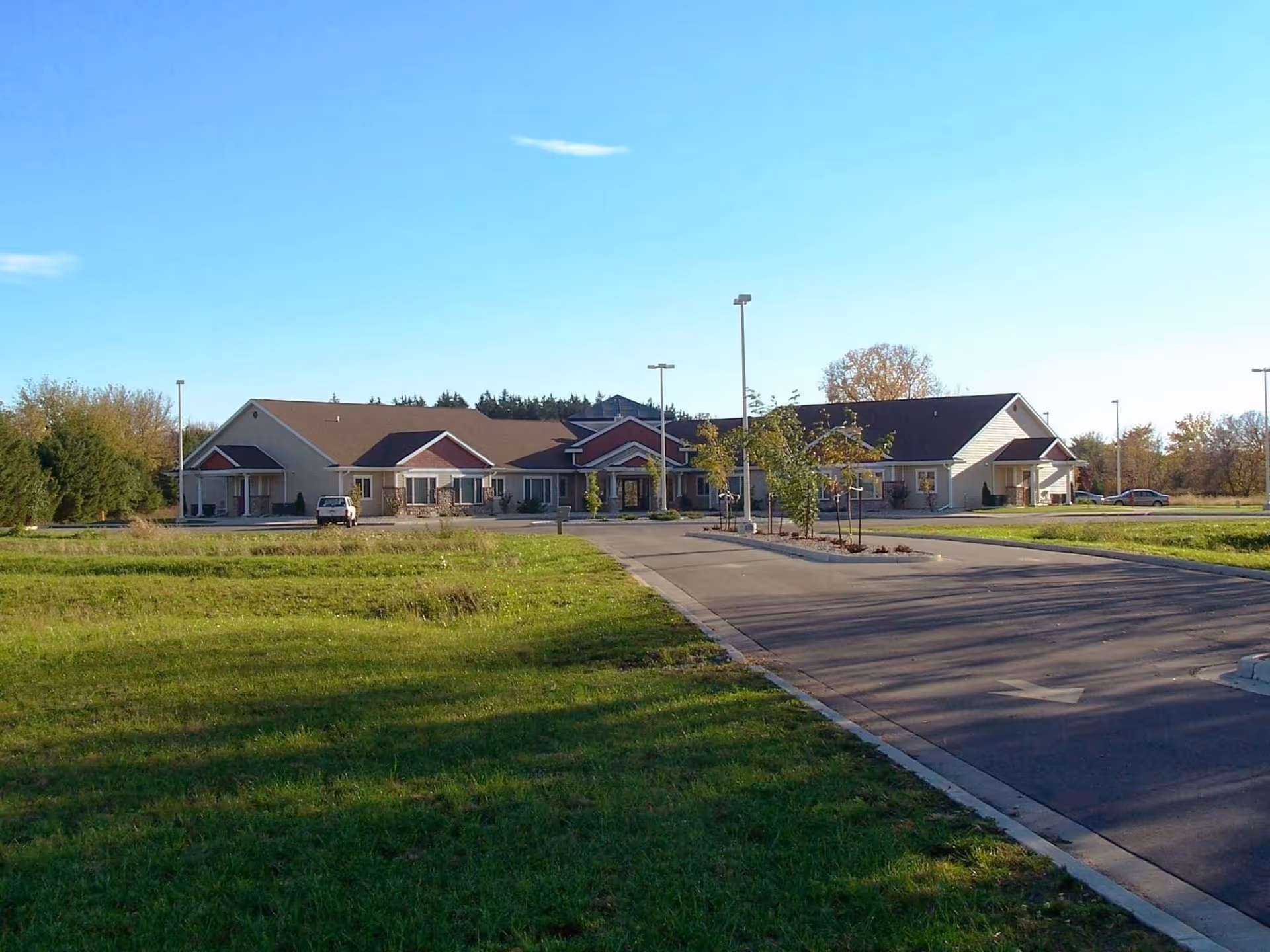 Exterior view of Oakwood Manor, a single-story building with a large parking area and green lawn in front under a clear blue sky.