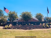 Landscaped entrance sign for Blakey Hall Retirement Community with American and Texas flags and shrubs.