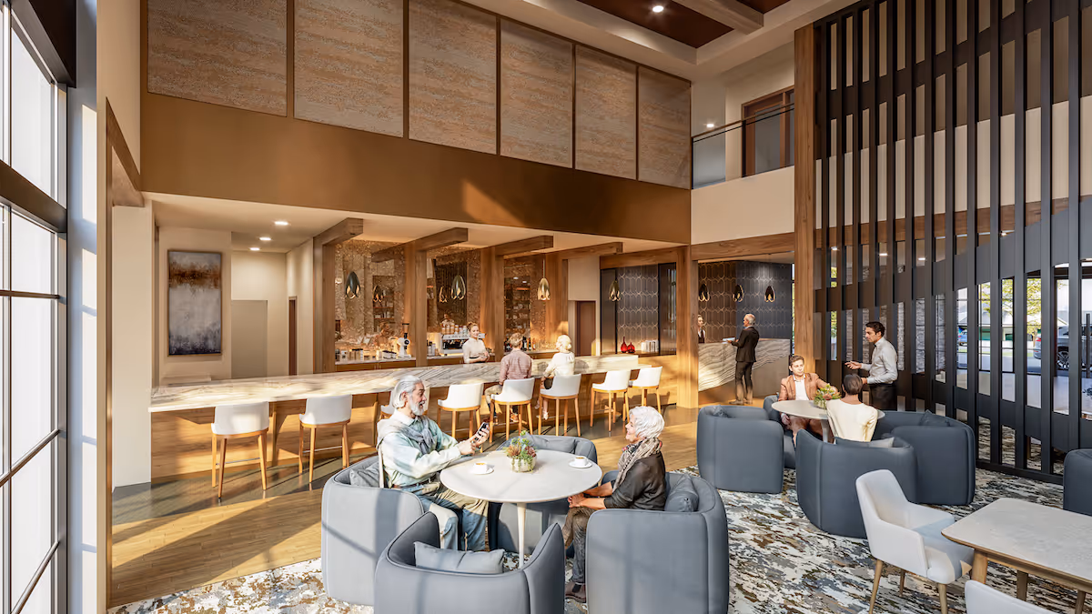A spacious and well-lit common area in a senior living facility featuring a high ceiling and large windows. Several elderly residents are seated in comfortable gray armchairs around small round tables, engaging in conversation. In the background, there is a long bar counter with white bar stools and staff members attending to guests. The room has warm wooden accents and modern decor, creating a welcoming atmosphere.