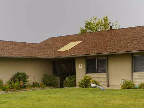 Single-story beige senior living facility with a grassy lawn and shrubs in front.