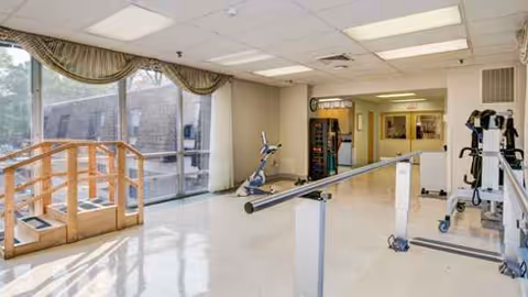 Bright rehab gym inside a senior facility with parallel bars and large windows.
