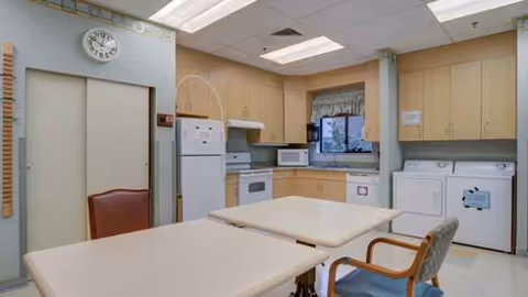 Communal kitchen and laundry area with tables, chairs, and appliances.