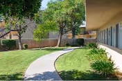 Curved concrete sidewalk winds through a green lawn beside a beige building with trees.