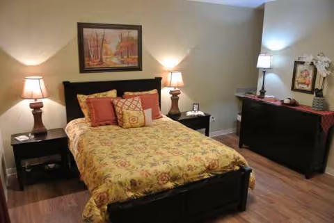 A cozy, well-lit bedroom with a floral bedspread, nightstands, and dresser in a senior facility.