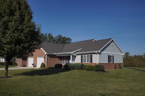 Single-story residential building with a combination of brick and white siding exterior, surrounded by a well-maintained lawn and a tree on the left side under a clear blue sky.