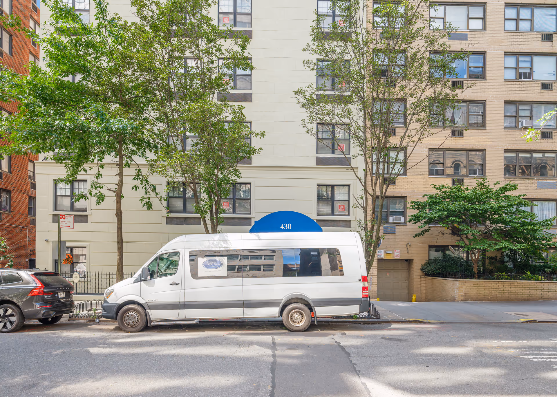 Street view of a residential building with a blue awning labeled 430, flanked by trees and parked vehicles including a white van and a black car.