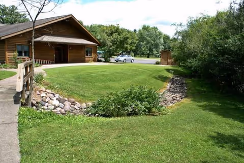 Exterior view of a wooden senior living facility with a manicured lawn and trees.