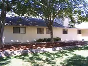 Front view of a single-story beige senior living building with trees and a lawn.