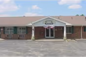 Front exterior of a single-story brick senior living building with a covered entrance displaying a 'Welcome' sign.