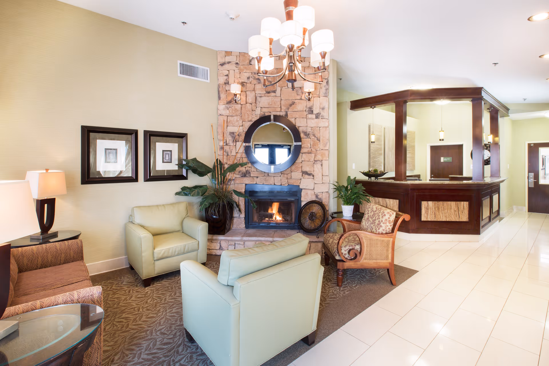 Bright reception lounge with armchairs around a stone fireplace and a wooden reception desk in the background.