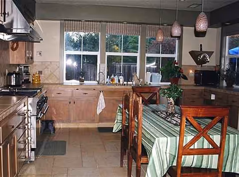 Bright kitchen with wooden cabinets, tiled floor, and a dining table by a large window.