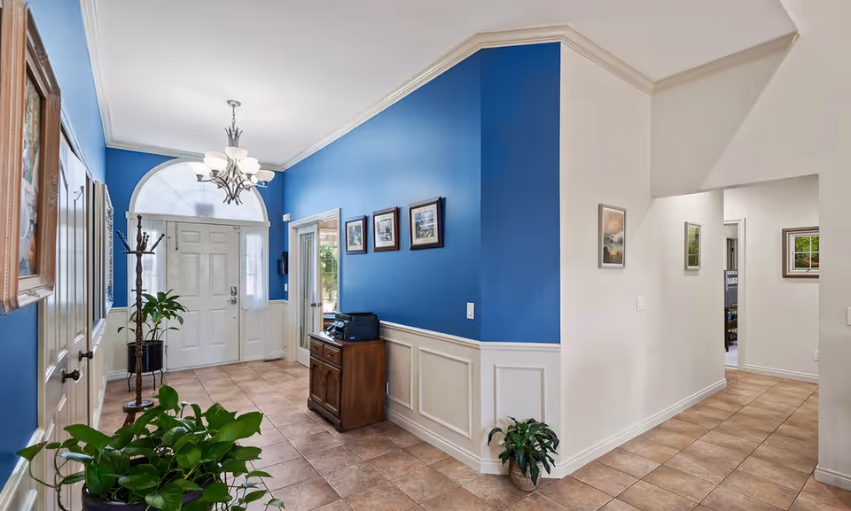 Bright entry foyer with a blue accent wall, white front door, chandelier, tiled floor, plants, and a wooden console table.