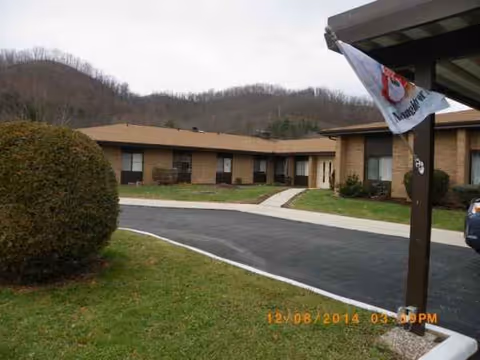 Exterior view of Nella's senior living facility with walkway, bushes, and a flag.