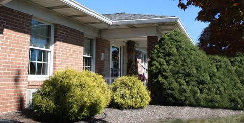 Brick senior living facility exterior with windows, entrance, and neatly trimmed shrubs.