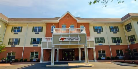 Front facade of a three-story assisted living building with a covered entrance and balcony.