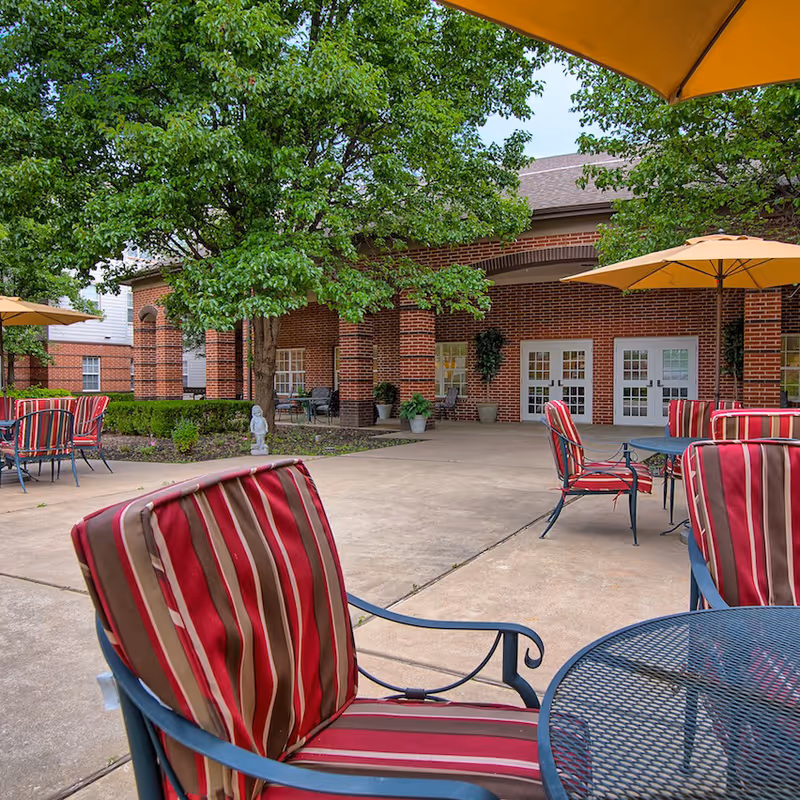 Outdoor brick courtyard with striped patio chairs, tables and yellow umbrellas in front of a building entrance.