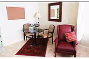 Small seating area with a round table, two chairs, a red armchair with a striped pillow, a floor lamp, and a wall mirror.