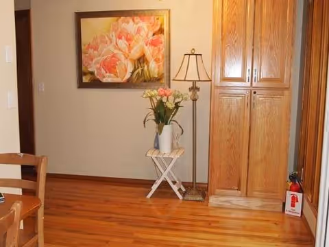 Cozy interior room featuring a floral painting, vase, floor lamp, and tall wooden cabinets.