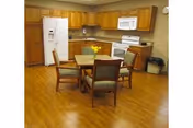 Open kitchen with wood cabinets, white appliances and a small square dining table with four chairs on hardwood flooring.