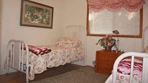 Two metal-framed beds with floral quilts, a dresser, and a window in a cozy bedroom.