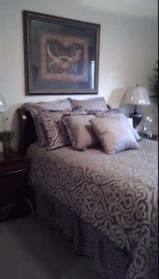 Cozy bedroom with a patterned bedspread and multiple pillows, nightstands with lamps, and framed artwork above the headboard.