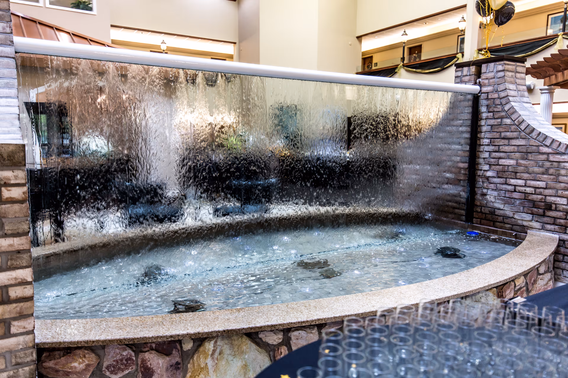 Indoor decorative cascading water wall and shallow pool with a stone and brick surround in a lobby area.