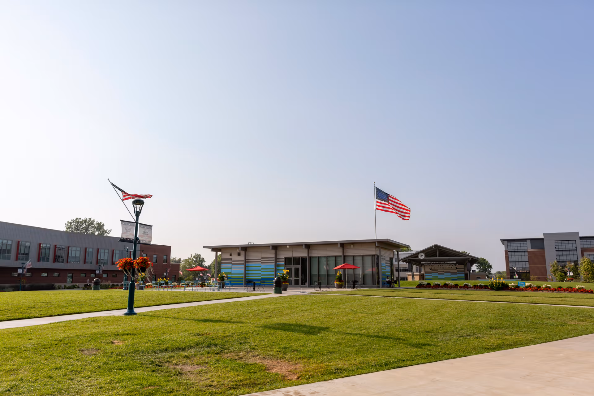 Green lawn and courtyard in front of a single-story modern senior living building with American flags and outdoor seating.