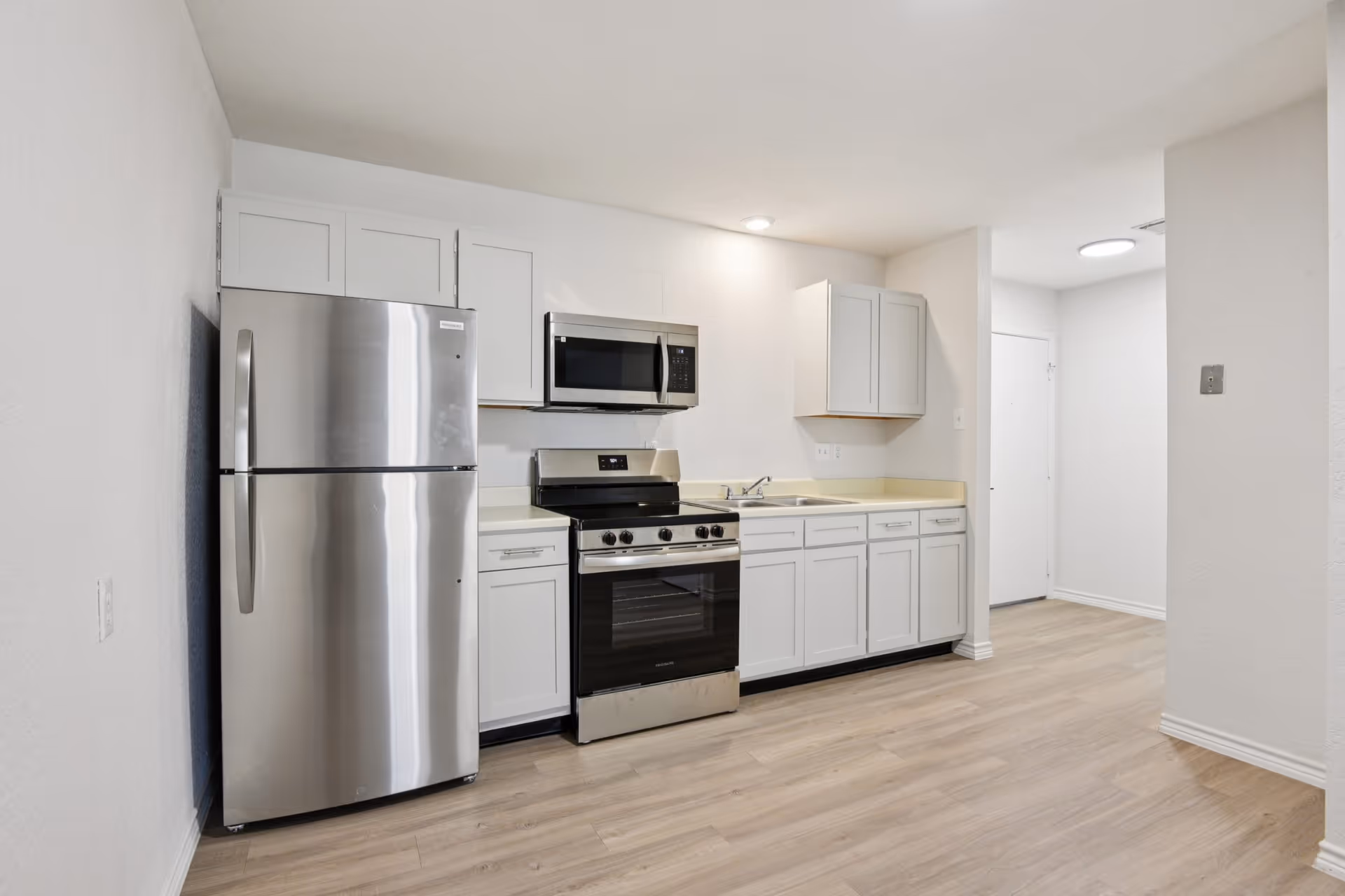 Modern kitchen with stainless steel refrigerator, stove, microwave, and white cabinets.